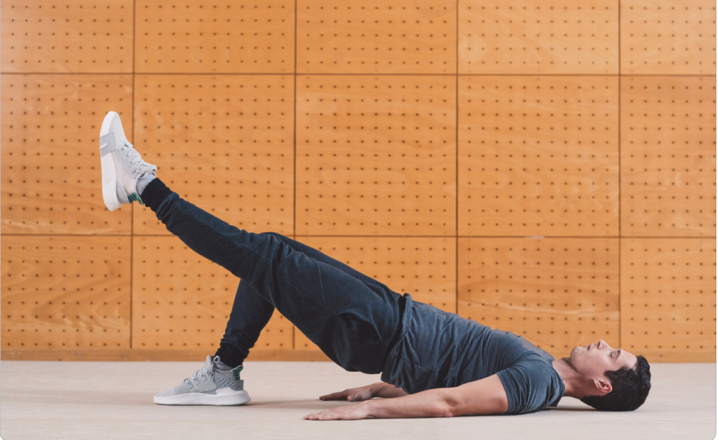 A young man performing an advanced glute bridge. The glute max is the largest postural muscle we have. Our posture muscles are often very weak in patients with cervical facet syndrome. 