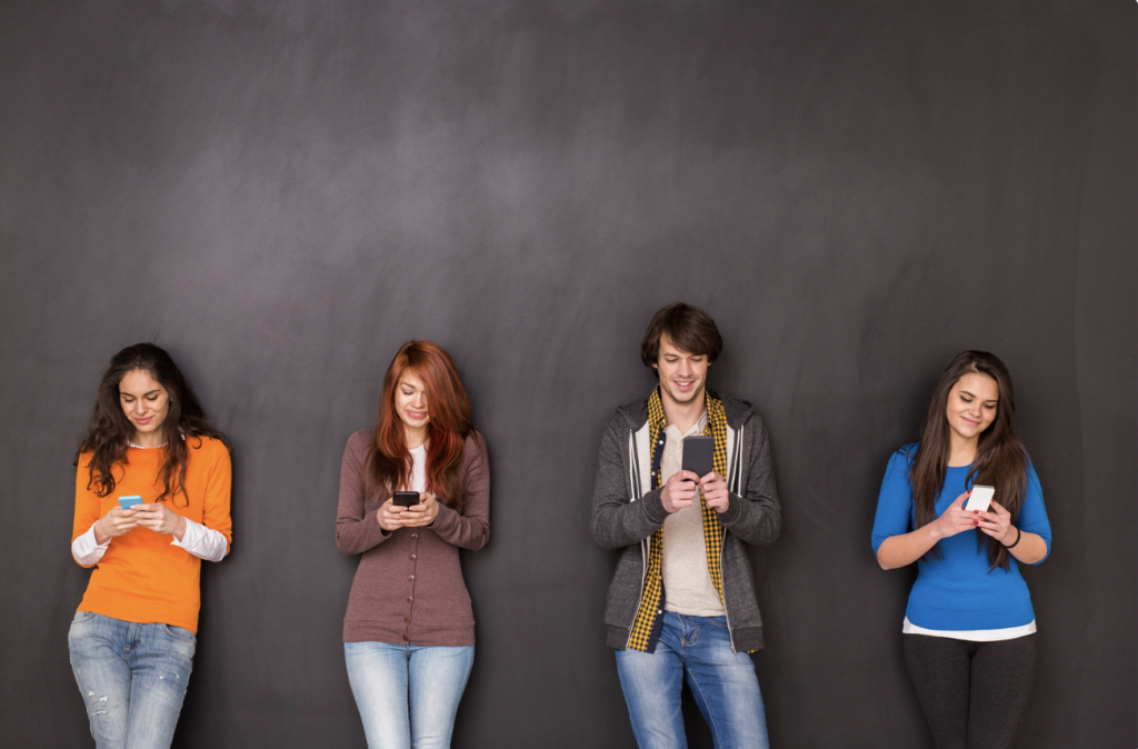 Four younger people texting which is one of the main leading causes to cervical facet syndrome