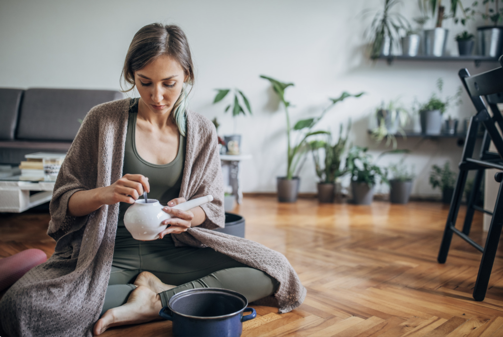 A young woman sitting on her floor preparing her neti pot to help relieve her congestion caused by allergies