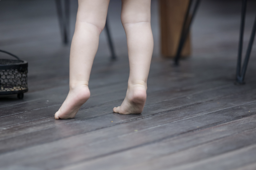 A child standing bare foot on the floor toe walking. 