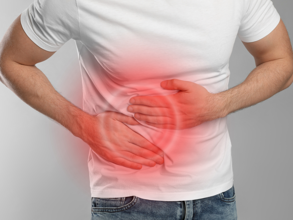 Male patient in white t-shirt holding right side of abdomen to demonstrate a gallbladder attack in 