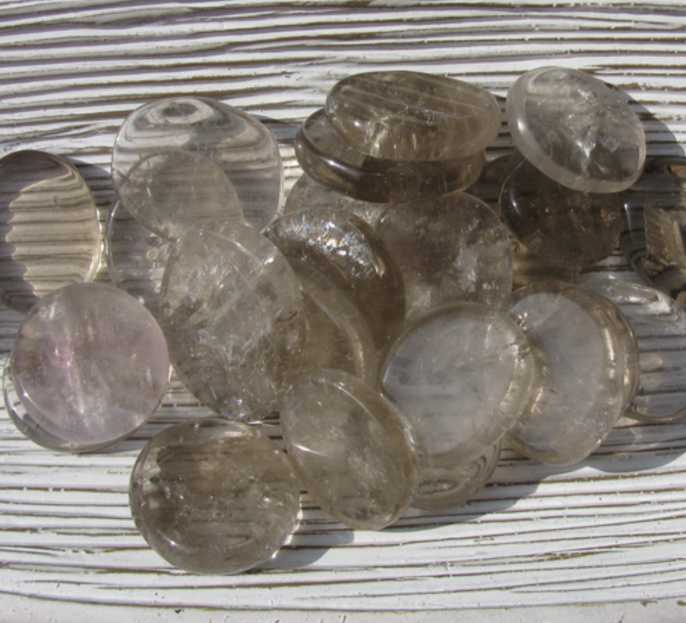 A lot of oval smoky quartz on a white counter. Smoky Quartz is a clear stone with a blackish hughe to it. 
