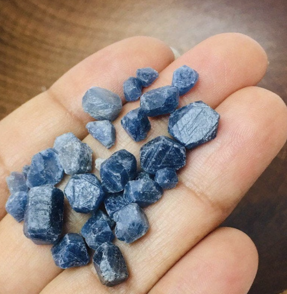 Multiple different sized blue sapphire stones in a woman's hand.