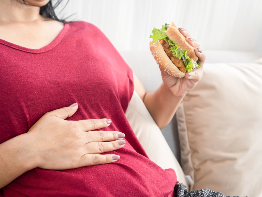 Woman with red shirt holding a sandwich and her upper abdomen to demonstrate similarities between gallbladder symptoms and acid reflux pain.